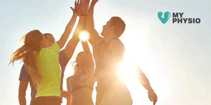 A group of active people giving a high-five outdoors in bright sunlight, symbolizing energy and teamwork, used by My Physio for promoting physiotherapy and wellness services